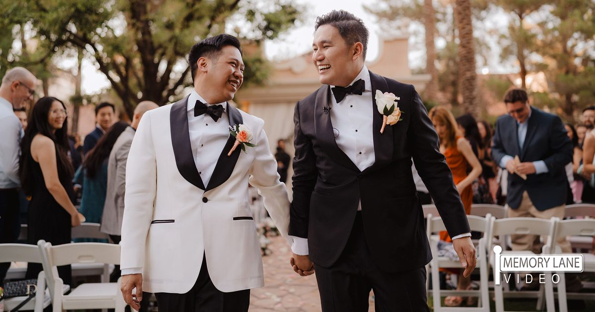 Two grooms laughing and holding hands during their wedding processional at a Las Vegas outdoor ceremony